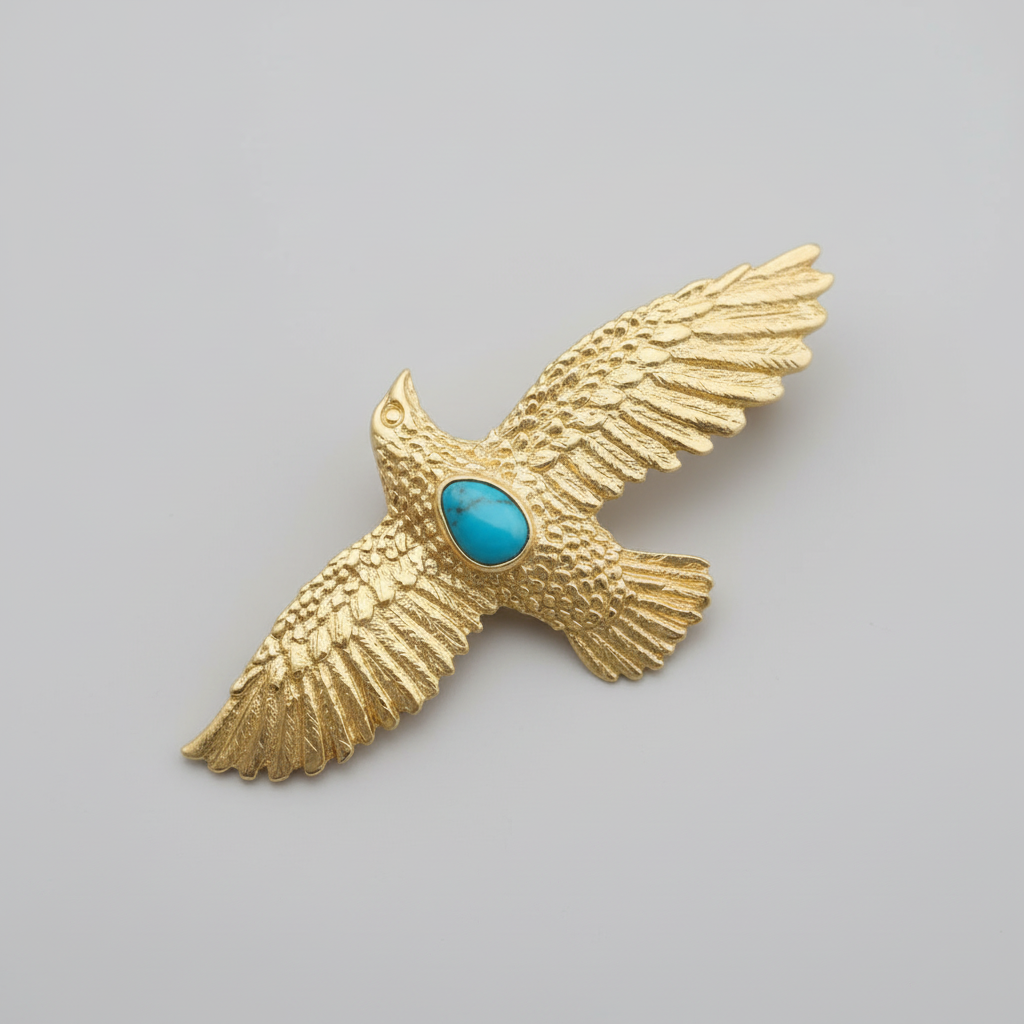 Gold eagle brooch with a turquoise stone on a gray background