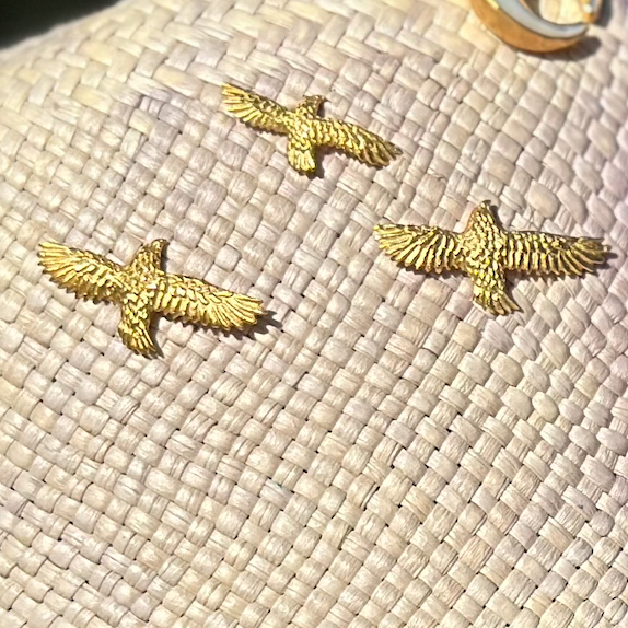 Three gold eagle pins on a textured beige surface